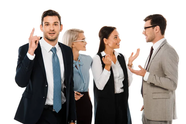 Exitoso hombre de negocios teniendo idea y apuntando hacia arriba mientras colegas discutiendo detrás aislado en blanco - foto de stock