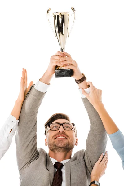 Exitoso hombre de negocios sosteniendo copa trofeo por encima de la cabeza mientras sus colegas tratan de aislarlo en blanco - foto de stock