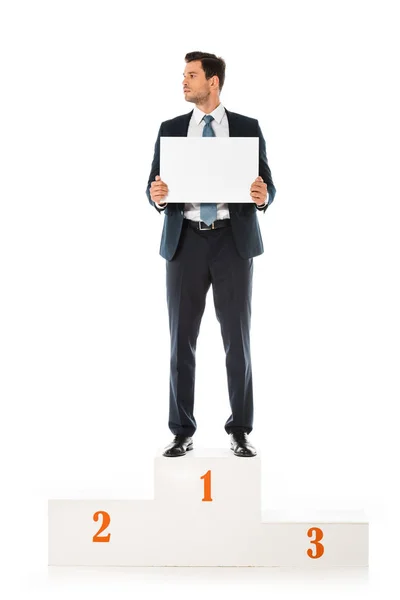 Homem de negócios bonito segurando cartaz em branco, enquanto em pé no pódio vencedores isolados em branco — Fotografia de Stock