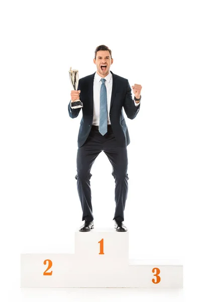 Excité homme d'affaires émotionnel avec coupe trophée debout sur le podium vainqueur isolé sur blanc — Photo de stock