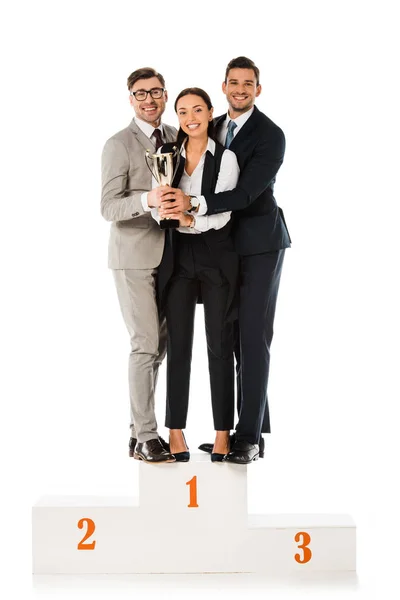 Equipe de negócios segurando copo de troféu enquanto em pé no pódio vencedores juntos isolados em branco — Fotografia de Stock