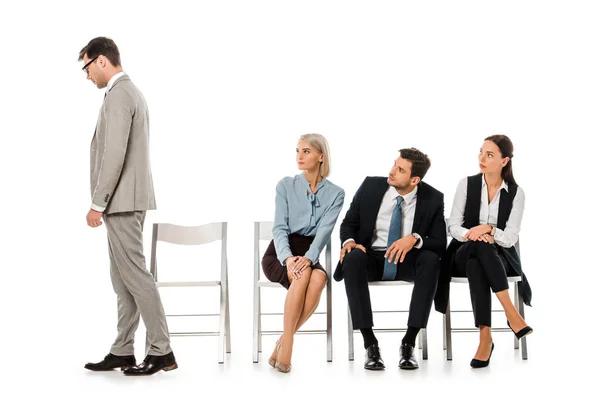 Fired businessman going away while colleagues sitting on chairs and looking at him isolated on white — Stock Photo