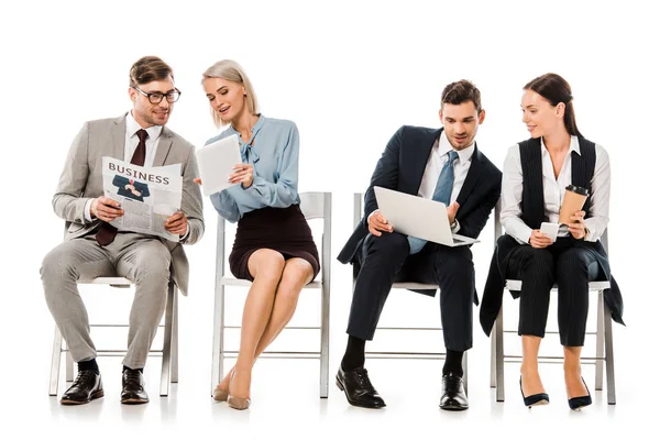 Empresarios sentados en sillas y discutiendo el trabajo con dispositivos digitales, aislados en blanco - foto de stock