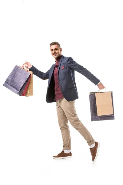 Lächelnder erwachsener männlicher Shopper in Jacke, der mit bunten Papiertüten auf weißem Grund läuft — Stockfoto