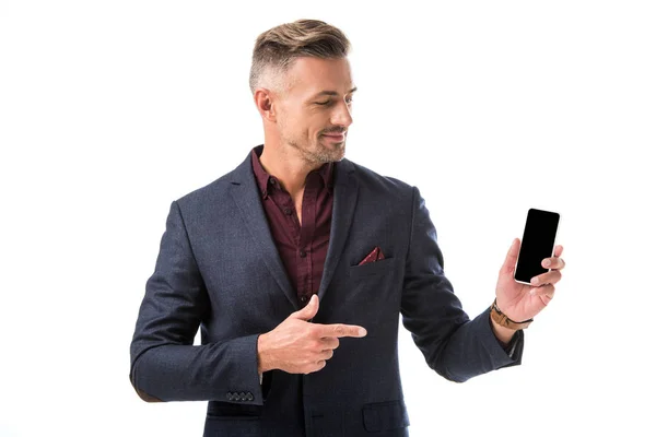 Adulto elegante hombre en chaqueta apuntando con el dedo en el teléfono inteligente con pantalla en blanco aislado en blanco - foto de stock