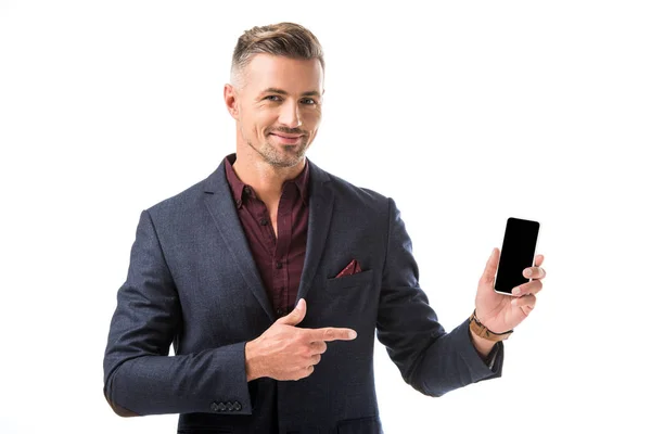 Позитивний дорослий стильний чоловік в куртці, вказуючи пальцем на смартфон з порожнім екраном ізольовано на білому — стокове фото
