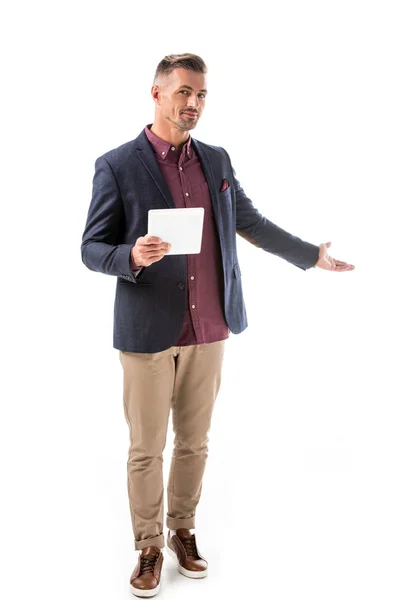Guapo hombre elegante en chaqueta celebración tableta digital y haciendo gesto de invitación aislado en blanco - foto de stock