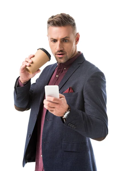 Homme élégant choqué avec tasse de café jetable en utilisant smartphone isolé sur blanc — Photo de stock