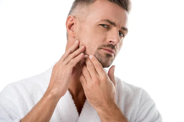 Hombre en albornoz comprobar la cara y preocuparse por su propia apariencia aislado en blanco - foto de stock