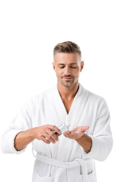 Hombre alegre en albornoz usando loción de afeitar aislado en blanco — Stock Photo