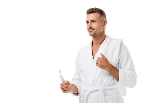 Man in bathrobe with towel over shoulder holding toothpaste and toothbrush isolated on white — Stock Photo