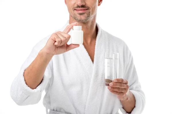 Partial view of adult man in bathrobe showing vitamins and holding glass of water isolated on white — Stock Photo