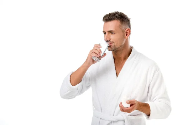 Uomo adulto in accappatoio prendere pillole con bicchiere d'acqua isolato su bianco — Foto stock