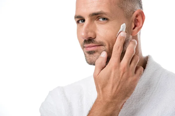 Erwachsene gut aussehende Mann im Bademantel Anwendung Schönheitscreme auf Gesicht isoliert auf weiß — Stockfoto