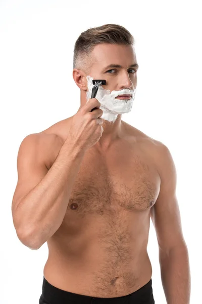 Serious muscular shirtless man with foam on face shaving with razor isolated on white — Stock Photo