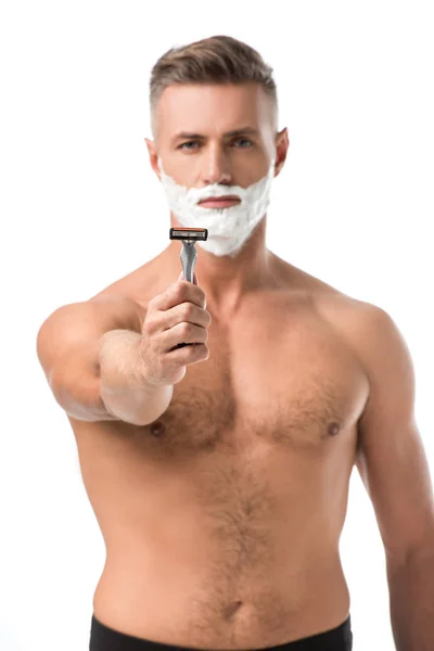 Selektiver Fokus muskulöser, hemdloser Mann mit Rasierschaum im Gesicht, der Rasiermesser isoliert auf Weiß zeigt — Stockfoto