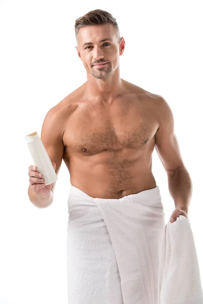 Hombre adulto feliz envuelto en toalla sosteniendo gel de ducha aislado en blanco - foto de stock