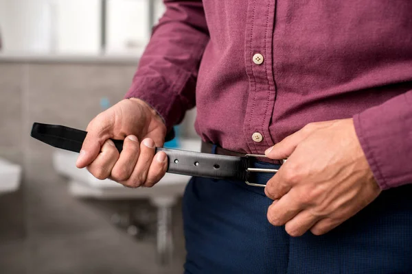 Cropped image of businessman putting on belt at home — Stock Photo