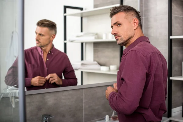 Enfoque selectivo de hombre de negocios adulto abotonamiento de la camisa en el baño en casa - foto de stock