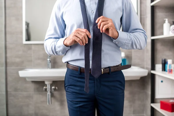 Обрезанный образ бизнесмена, связывающего галстук в ванной комнате — стоковое фото