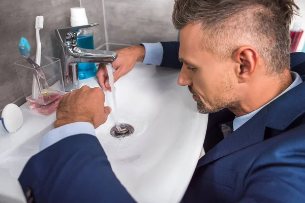 Seitenansicht eines erwachsenen Geschäftsmannes im Anzug, der vor dem Waschbecken im Bad sitzt — Stockfoto