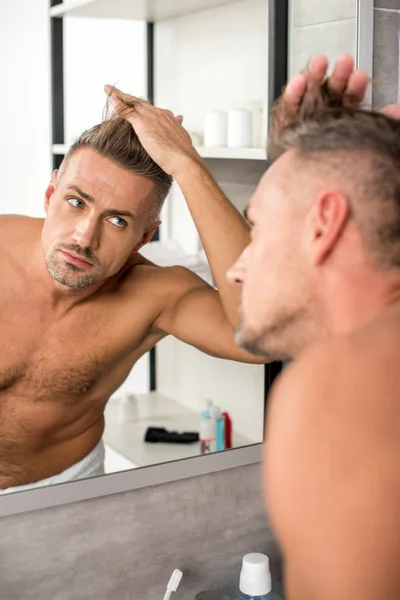 Messa a fuoco selettiva dell'uomo adulto che regola il taglio di capelli e guarda lo specchio in bagno — Foto stock