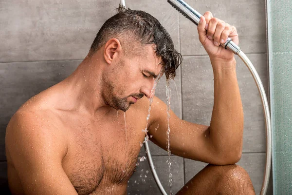 Вид сбоку взрослого мужчины с мышечным туловищем, принимающего душ по утрам — стоковое фото