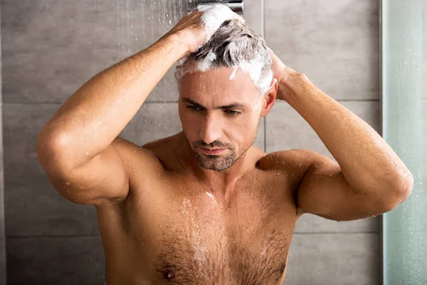 Selective focus of adult man washing hair with shampoo and taking shower — Stock Photo