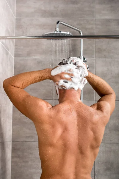 Rückansicht eines Mannes, der sich die Haare mit Shampoo wäscht und duscht — Stockfoto