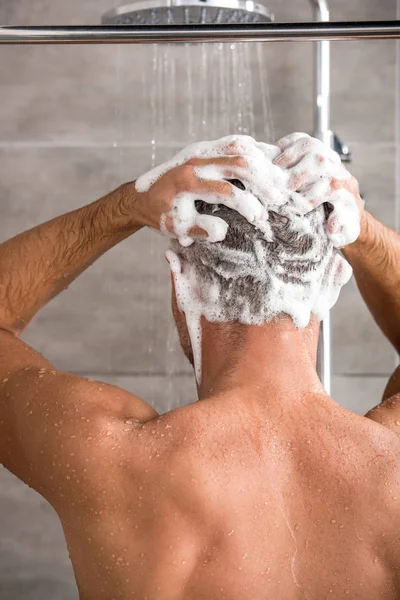 Rear view of man washing hair with shampoo and taking shower — Stock Photo