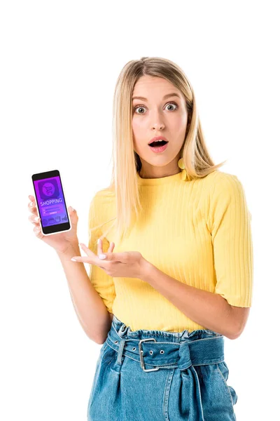 Sorprendió a la joven mujer sosteniendo el teléfono inteligente con la aplicación de compras en la pantalla y mirando a la cámara aislada en blanco - foto de stock