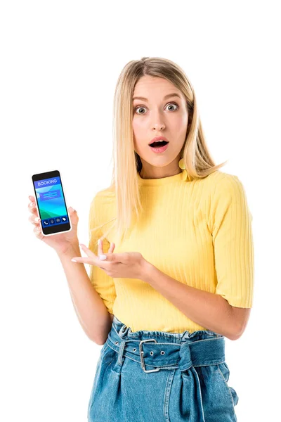 Scioccato giovane donna in possesso di smartphone con applicazione di prenotazione sullo schermo e guardando la fotocamera isolata su bianco — Foto stock