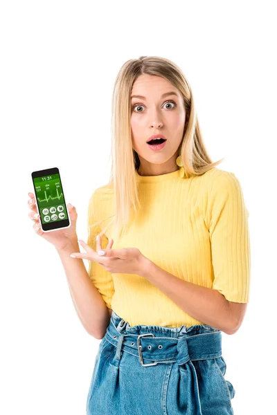 Шокированная молодая женщина держит смартфон с приложением здравоохранения на экране и глядя на камеру, изолированную на белом — стоковое фото