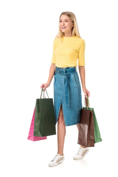 Vista completa de la joven sonriente sosteniendo bolsas de compras y mirando hacia otro lado aislado en blanco - foto de stock