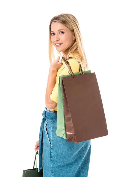 Attraente giovane donna che tiene borse della spesa e sorridente alla fotocamera isolata su bianco — Foto stock