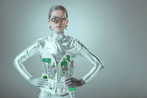 Cyborg plata futurista de pie con las manos en la cintura y mirando a la cámara aislada en gris, el concepto de la tecnología del futuro - foto de stock