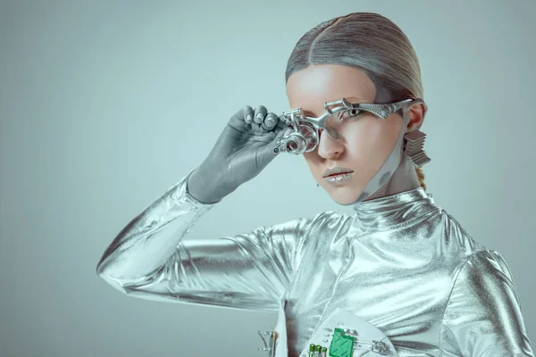 Futuristic silver cyborg adjusting eye prosthesis and looking at camera isolated on grey, future technology concept — Stock Photo