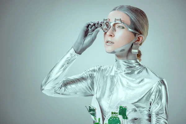 Robô de prata futurista ajustando prótese ocular e olhando para longe isolado no conceito de tecnologia cinza, futuro — Fotografia de Stock