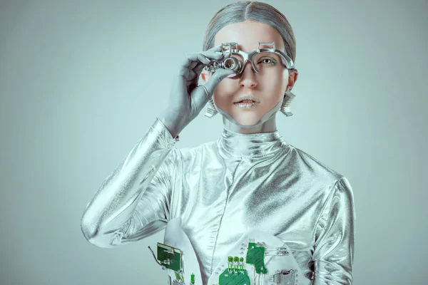 Robot argenté futuriste ajustant la prothèse oculaire et regardant la caméra isolée sur gris, concept technologique futur — Photo de stock