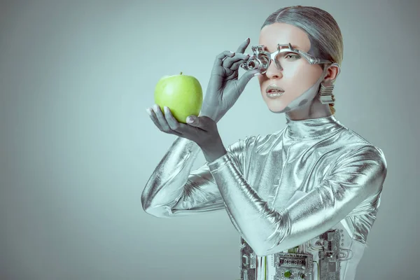 Робот рассматривает зеленое яблоко изолированы на сером, концепции технологии будущего — стоковое фото