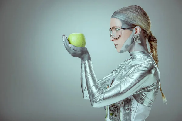 Vista laterale della donna robot tenendo mela verde isolato su grigio, concetto di tecnologia futura — Foto stock