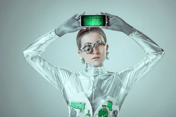 Silberner Roboter hält Smartphone mit Gerät über Kopf isoliert auf grauem, zukünftigem Technologiekonzept — Stockfoto