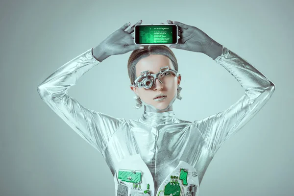 Silver robot holding smartphone with appliance above head isolated on grey, future technology concept — Stock Photo