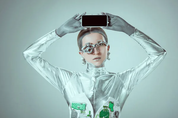 Silver robot holding smartphone with blank screen above head isolated on grey, future technology concept — Stock Photo