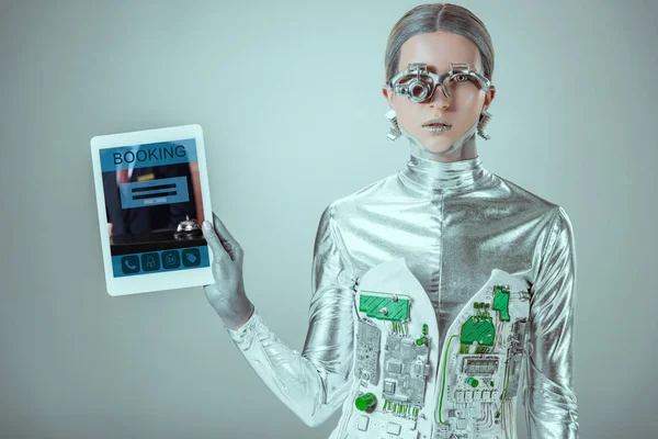 Silberner Roboter hält Tablet mit Buchungsgerät isoliert auf grauem, zukünftigem Technologiekonzept — Stockfoto