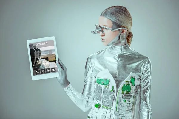 Robot plateado mirando la tableta con los boletos electrodomésticos aislados en gris, el concepto de la tecnología futura - foto de stock