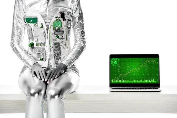 Imagem cortada do robô sentado na mesa perto do laptop com aparelho gráfico isolado no conceito de tecnologia branca e futura — Fotografia de Stock