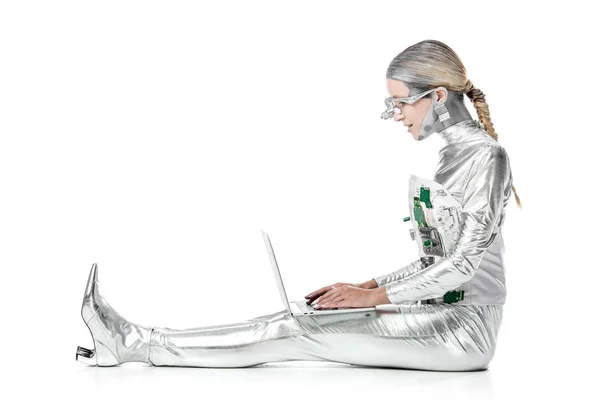 Side view of silver robot sitting and using laptop isolated on white, future technology concept — Stock Photo