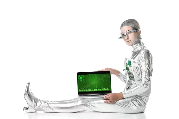 Robot plateado sentado y mostrando portátil con aparato gráfico aislado en blanco, concepto de tecnología futura — Stock Photo