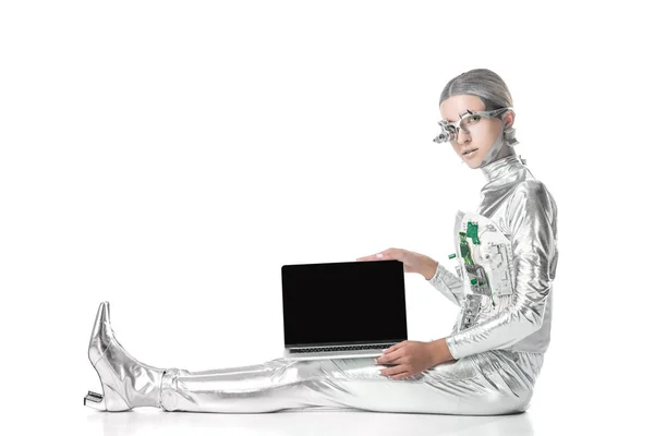 Robot d'argento seduto e mostrando laptop con schermo vuoto isolato su bianco, concetto di tecnologia futura — Foto stock
